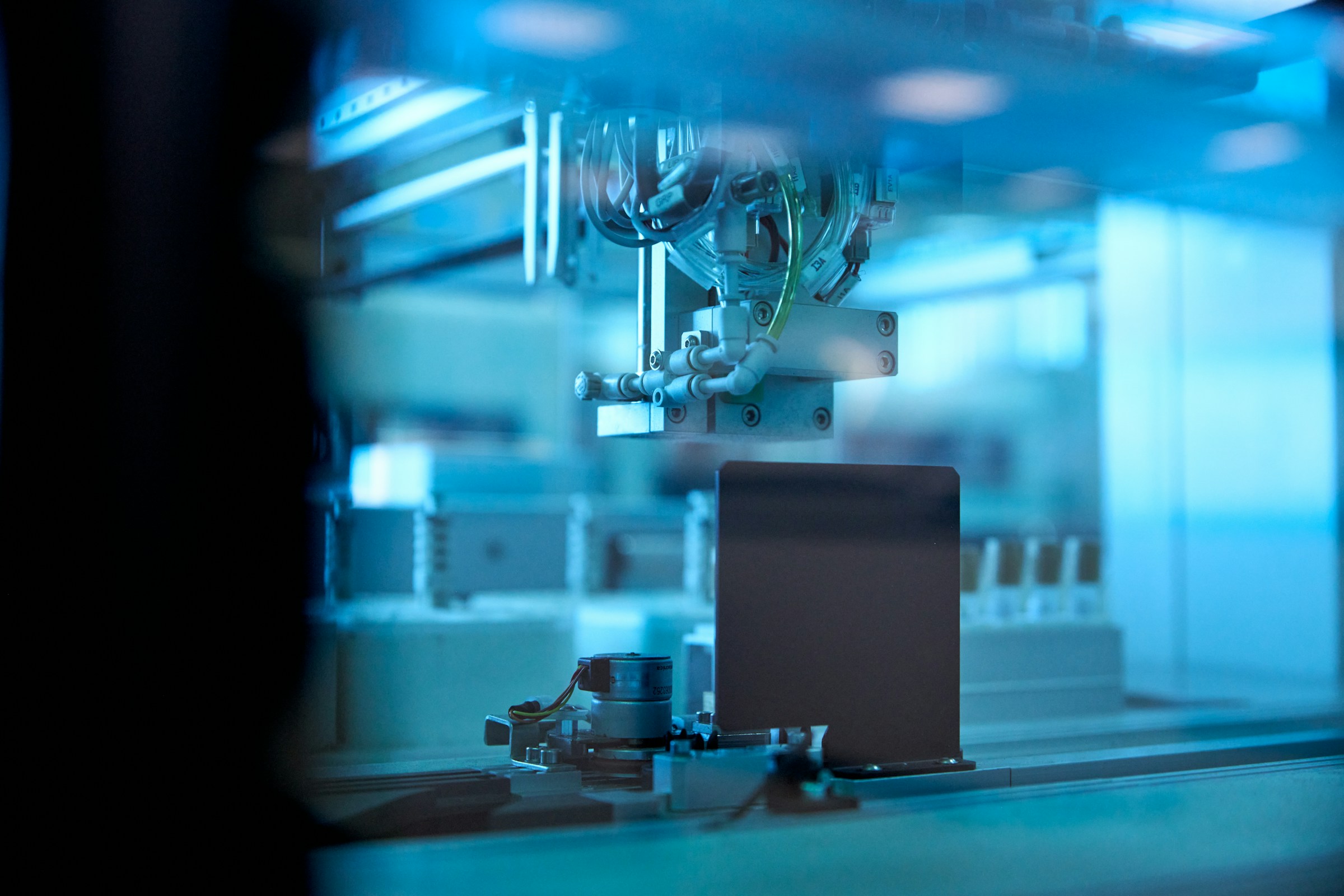Close-up of an automated machine with tubes and metal components inside a blue-lit industrial environment.